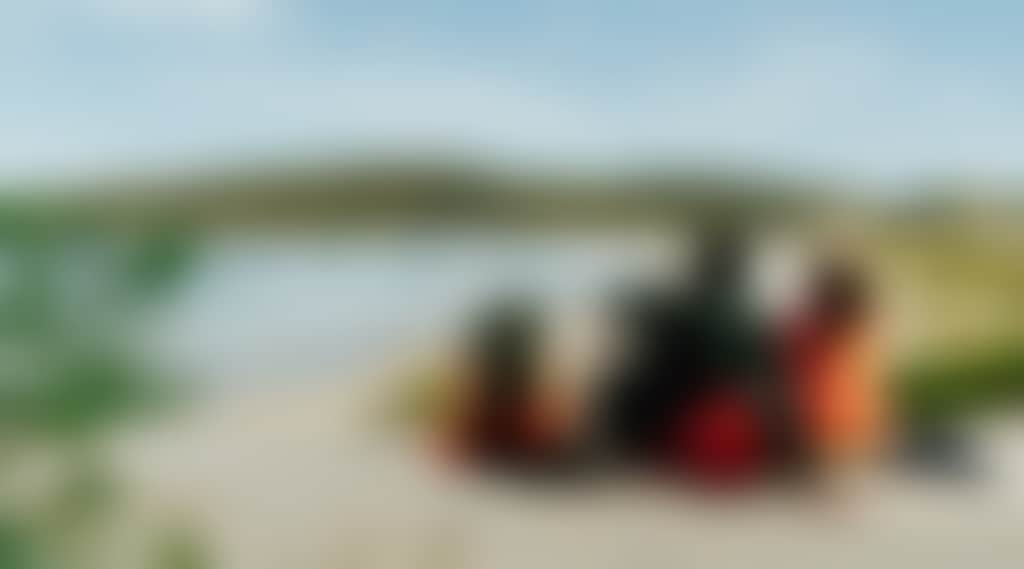 Hikers sitting on a sand dune overlooking a beach and green coastal headland