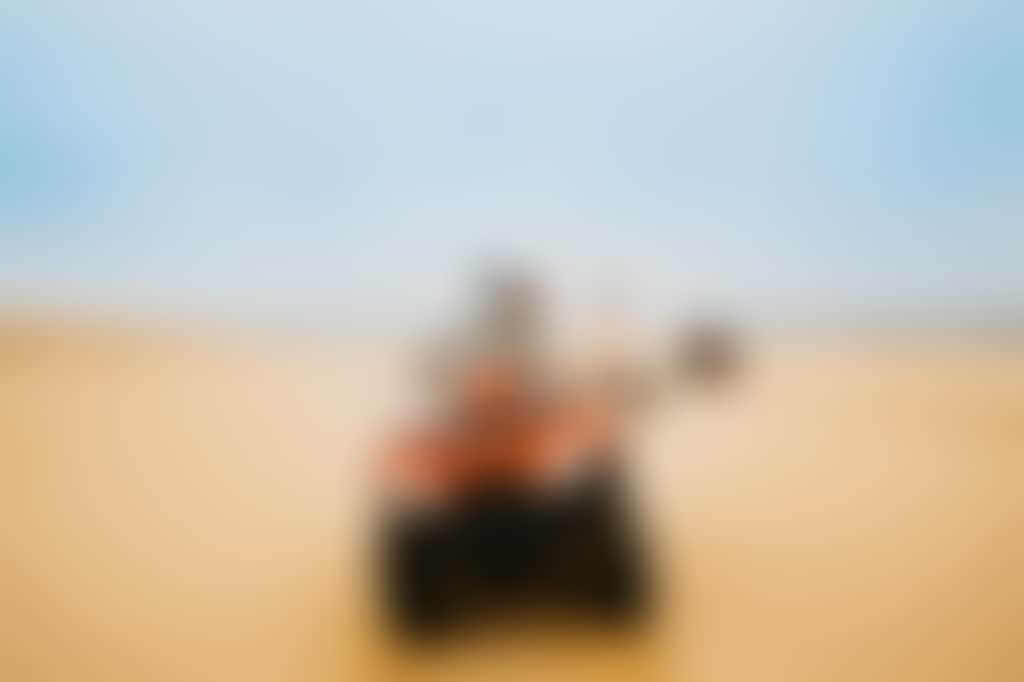 Convoy of three quad bikes rides in a line across sand dunes in port stephens